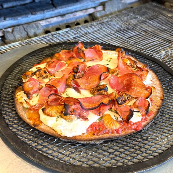 A freshly baked pizza with prosciutto, cheese, and figs on a metal grill.