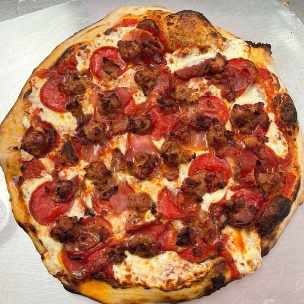 A freshly baked pizza with pepperoni, sausage, and ham, glistening with melted cheese and sauce.