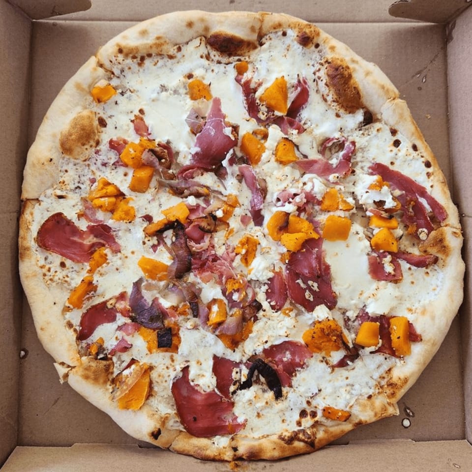 White sauce pizza with butternut squash, prosciutto, and red onion in a cardboard box.