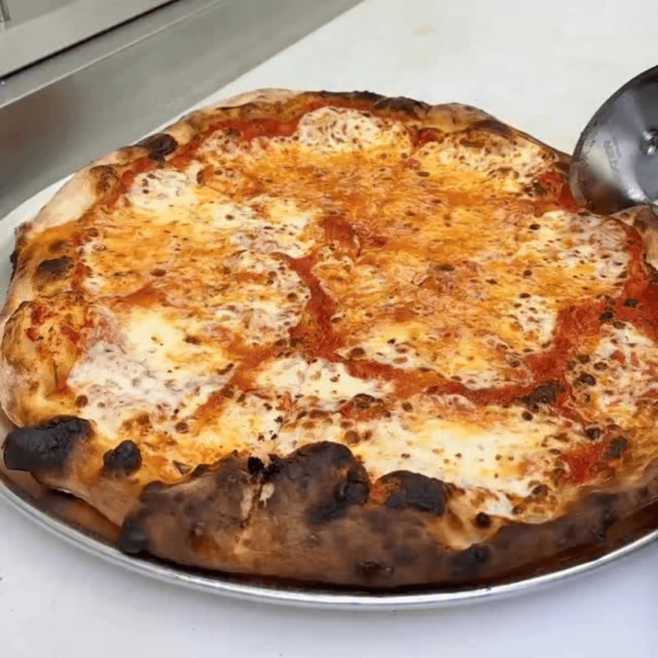 A freshly baked cheese pizza with a bubbly crust and melted mozzarella, being cut with a pizza cutter.