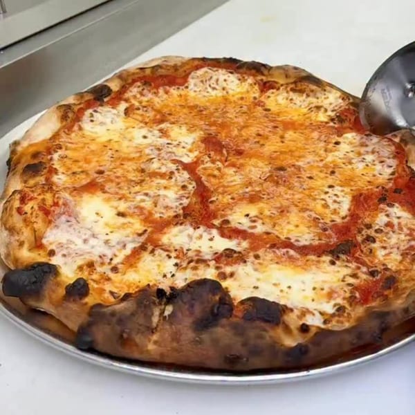 A freshly baked cheese pizza with a bubbly crust being cut on a metal tray.